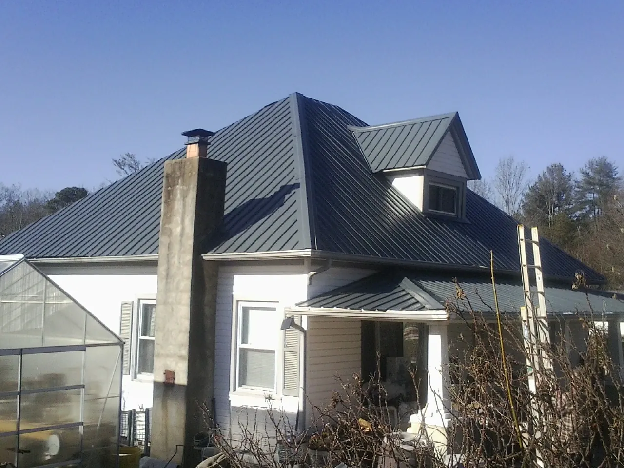 Dark blue standing seam metal roof on a white farmhouse with dormer — Slate & Tile Roof Repair by Roofing Brothers in Village Mills