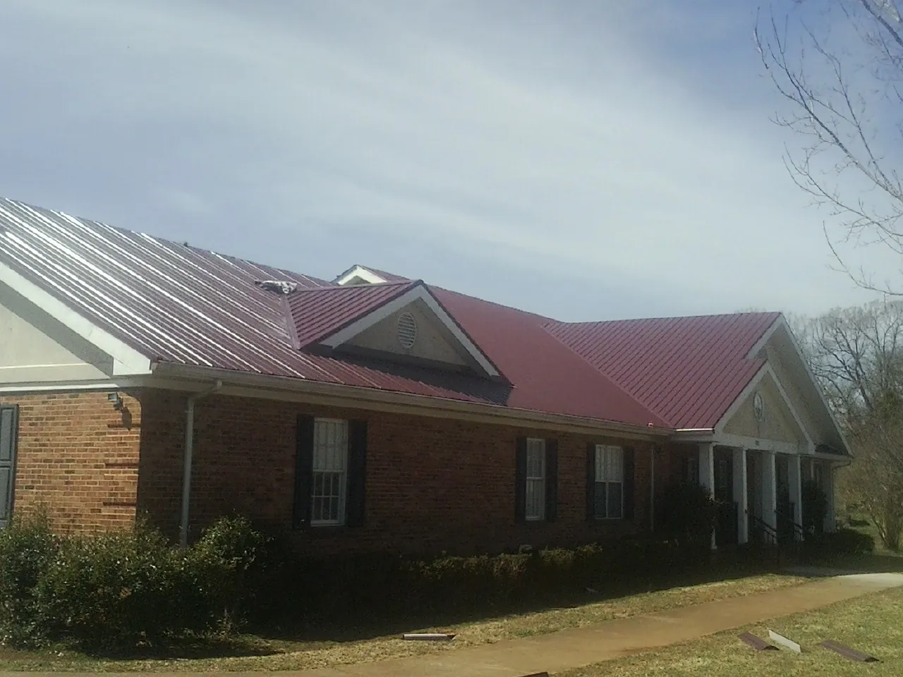 Red metal roof with gabled entries on a long brick building, from a Hail Damage Roof Repair job in Village Mills