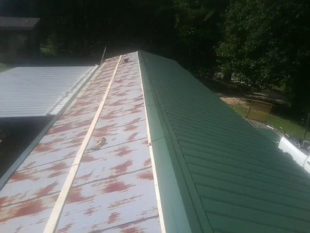Old rusted panels beside newly installed green metal roofing — Wind Damage Roof Repair by Roofing Brothers in Village Mills