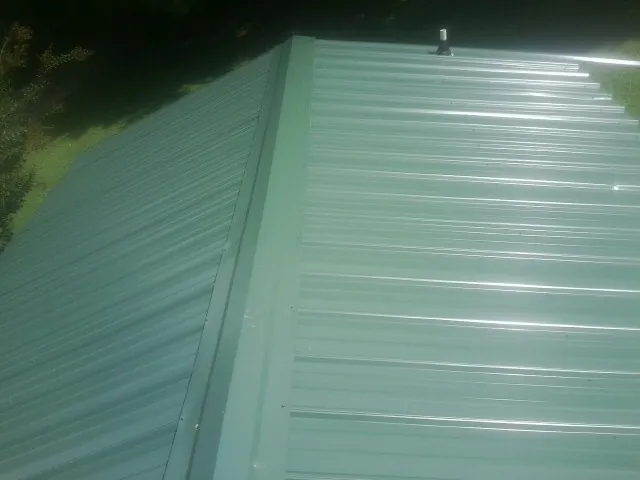 New green metal panels meeting at the ridge of a roof — Flat Roof Repair work by our crew in Village Mills