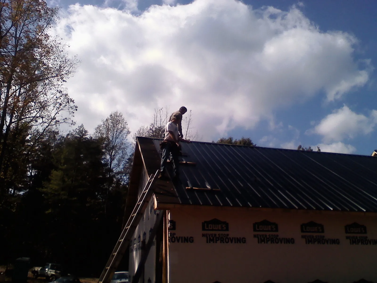 Roofer fastening dark metal panels high against a cloudy sky, from a Roof Inspection job in Village Mills