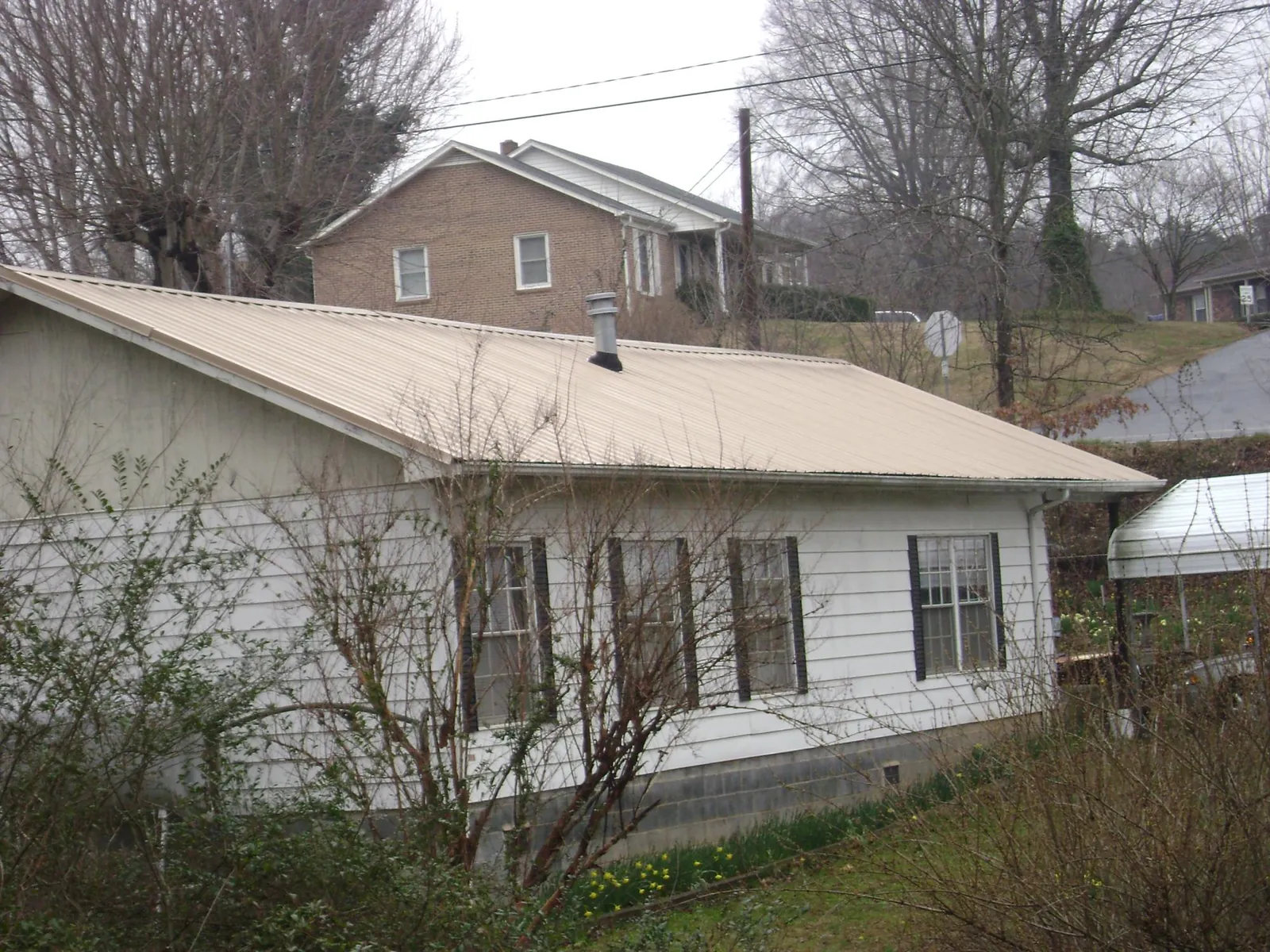 Tan metal roof on a white sided house set into a hillside — Commercial Roofing by Roofing Brothers in Village Mills