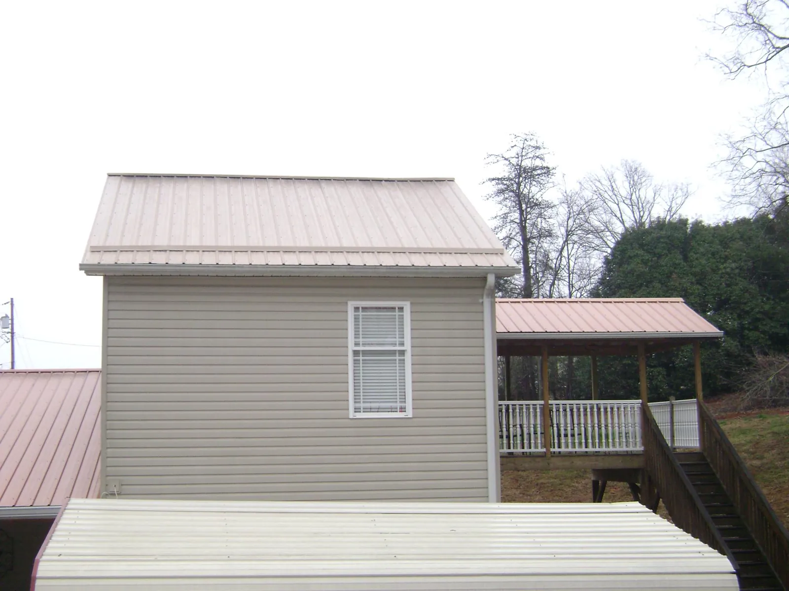 Tan metal roofs on a two story addition and attached porch, from a Roof Replacement job in Village Mills